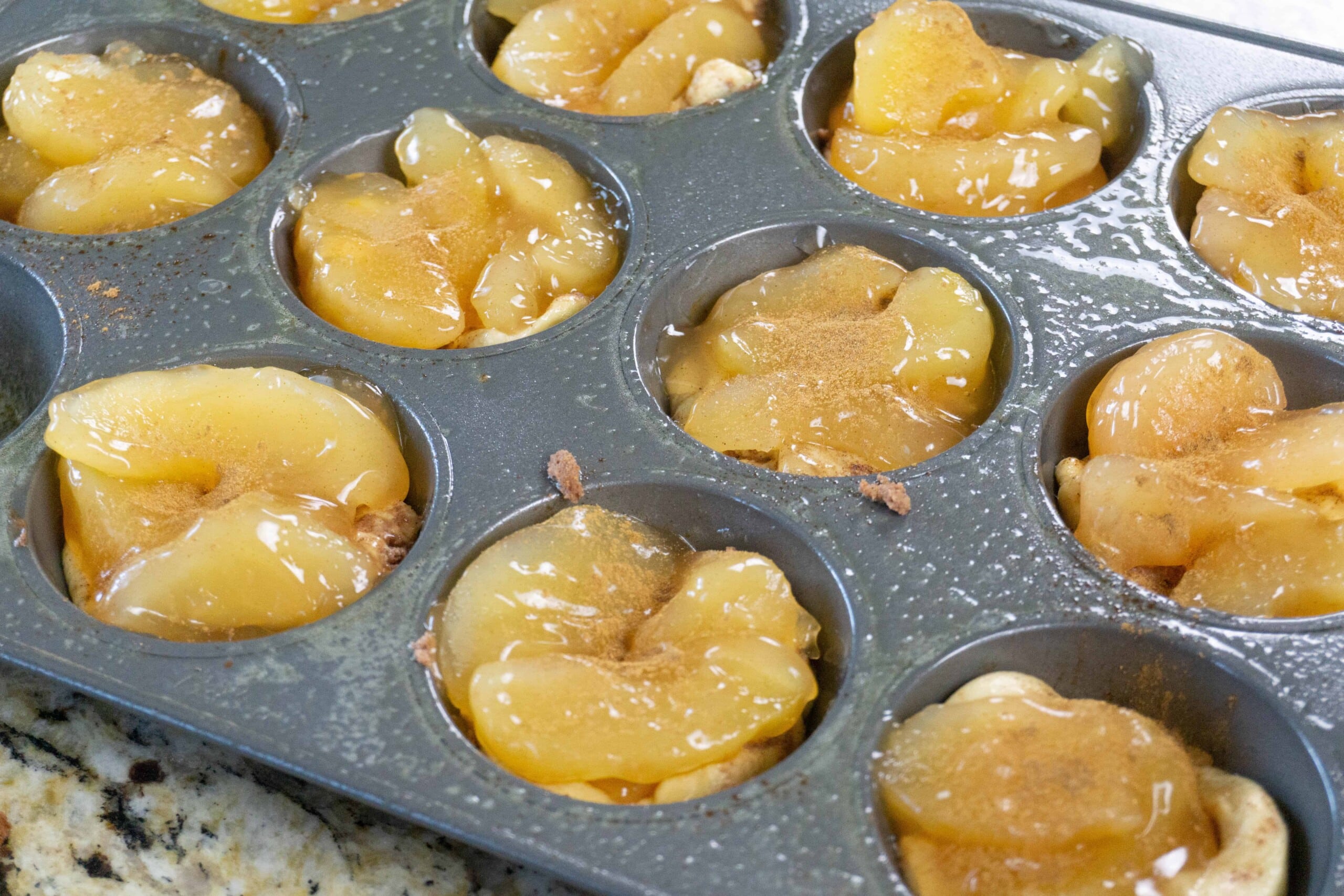 Muffin tin with cinnamon roll dough and apple filling - apple cinnamon muffins