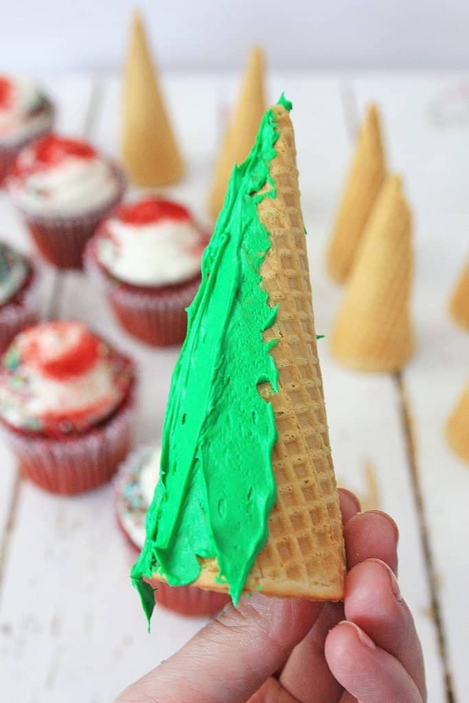 Ice cream cone being iced with green icing to create a Christmas tree.
