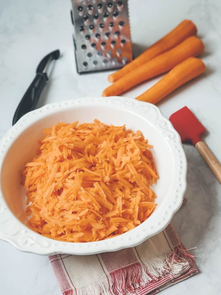 Shredded carrots in a white bowl on counter top before being added to carrot cake batter.