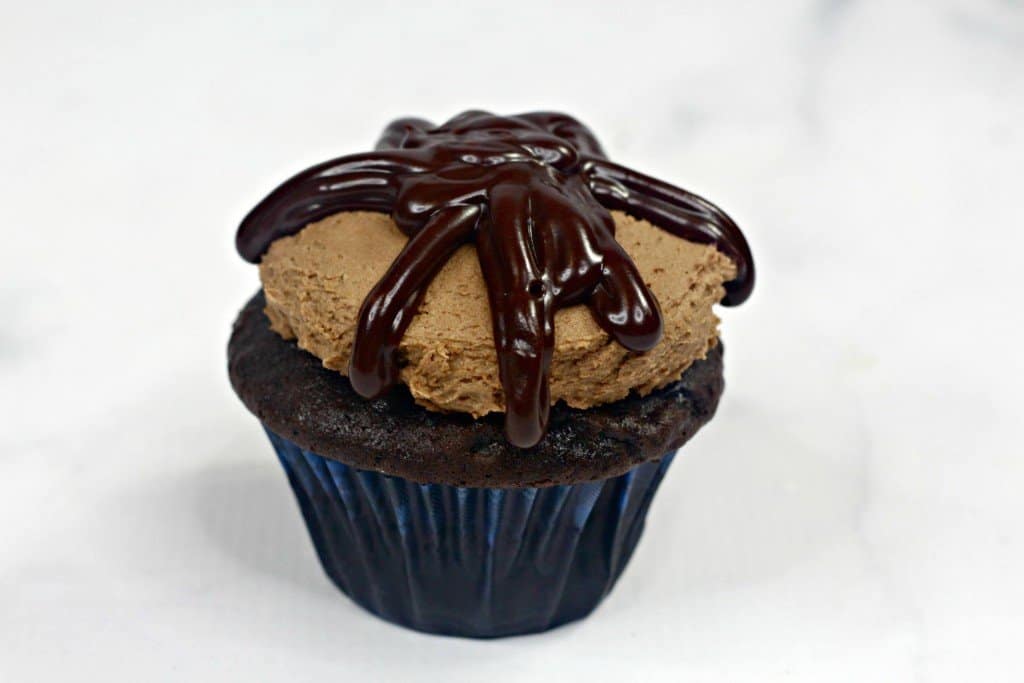 Chocolate cupcake iced with homemade chocolate frosting on marble countertop with ganache added on top