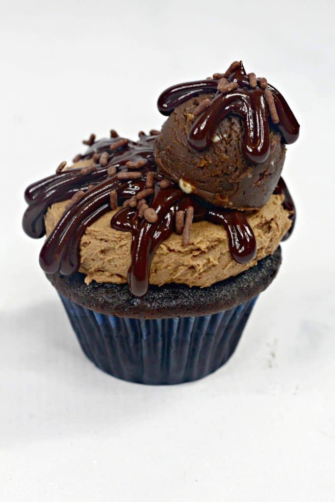 Chocolate cupcake iced with homemade chocolate frosting on marble countertop with ganache and cookie dough on top.