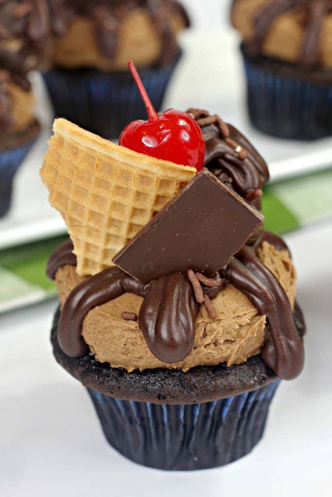 Chocolate cupcake iced with homemade chocolate frosting on marble countertop with ganache and cookie dough on top.