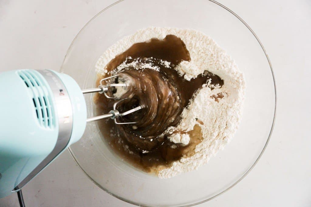 Icing ingredients in glass mixing bowl being combined with hand mixer.