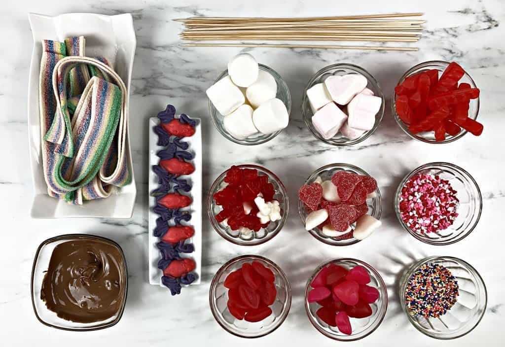 Various candy options for candy kabobs, set out in dishes on marble countertop