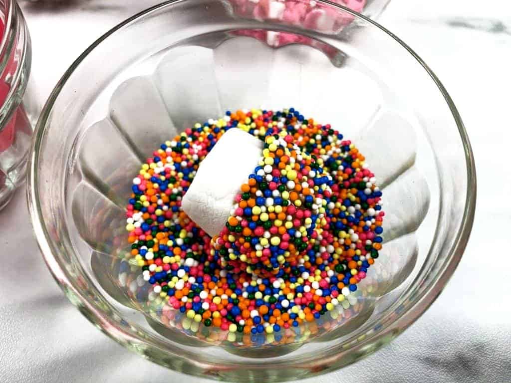 Marshmallow in a bowl of sprinkles, being covered to be added to candy kabobs.