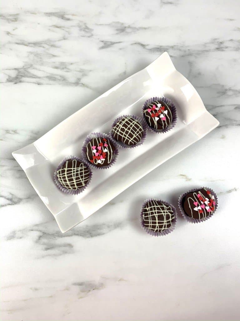 Beautiful oreo balls finished and displayed on white serving dish with 2 on countertop.
