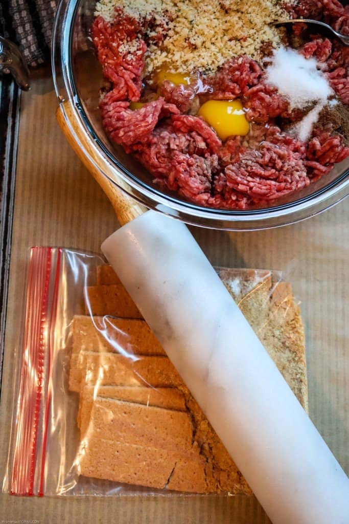 Swedish meatball ingredients being combined in glass mixing bowl. Rolling pin being used to crush graham crackers in ziploc bag.