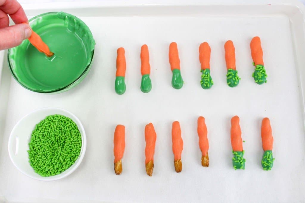 Green chocolate melts with pretzel being dipped to make carrot patch pudding cups.