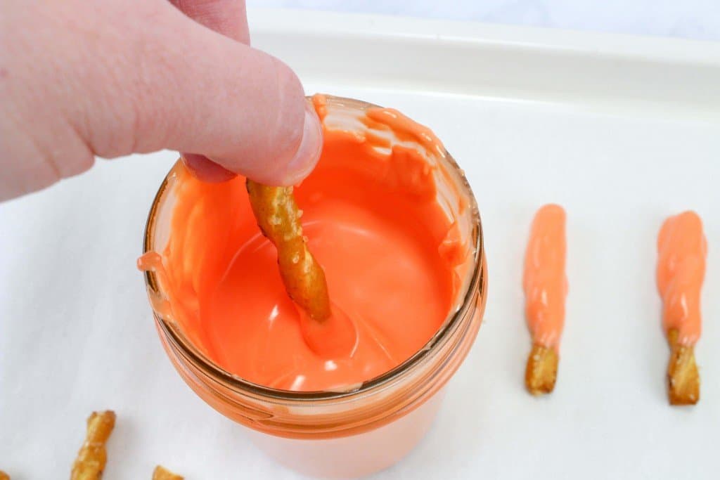 Orange chocolate melts with pretzel being dipped to make carrot patch pudding cups.