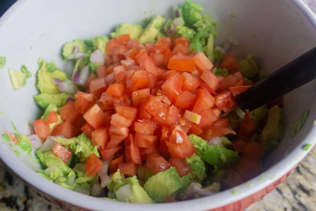 Hand smashed guacamole being mixed with tomatoes.