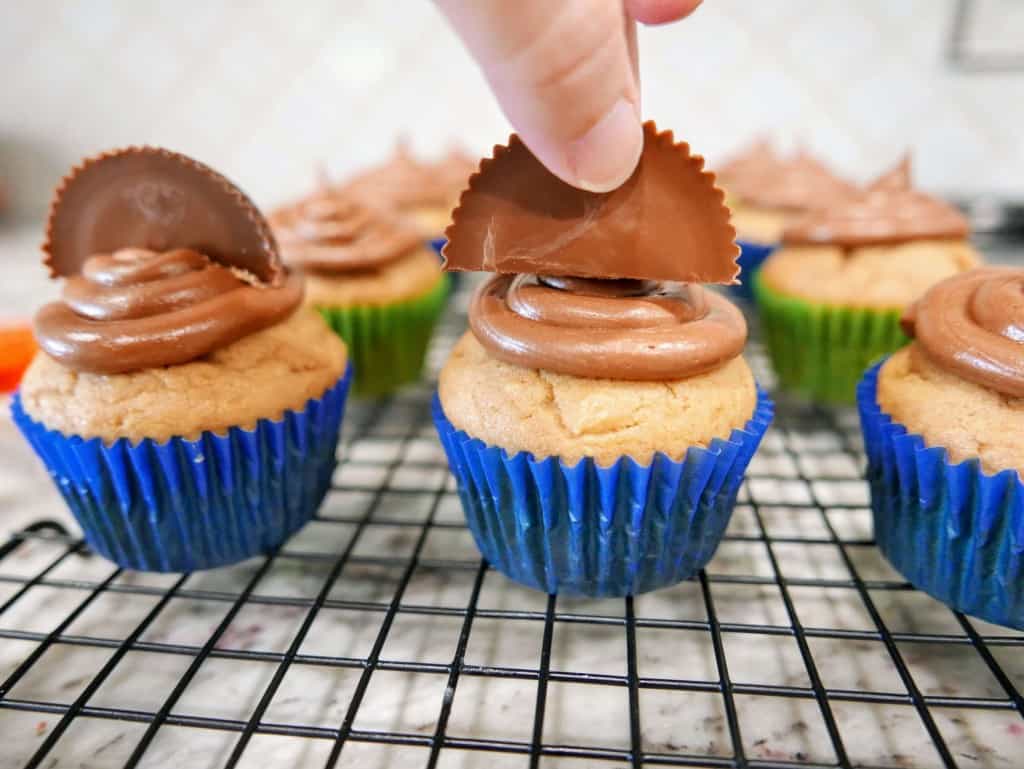 Nutella Cupcakes after being iced on wire cooling rack with Reese's peanut butter cups being placed on top of each.